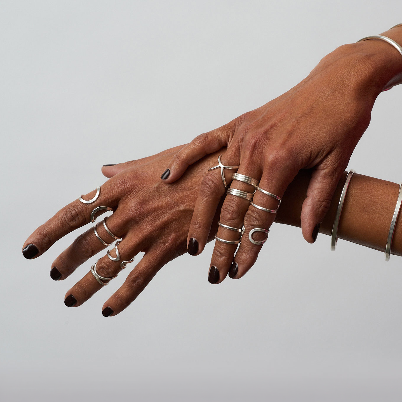 Two hands with multiple rings on a plain background